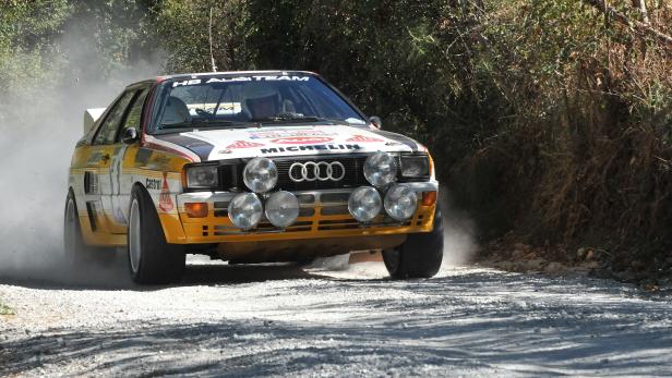 Ein Audi Quattro Rallye-Wagen fährt auf einer Schotterstraße.