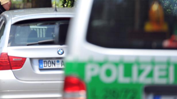 Ein silberner BMW steht neben einem unscharfen Polizeiwagen.