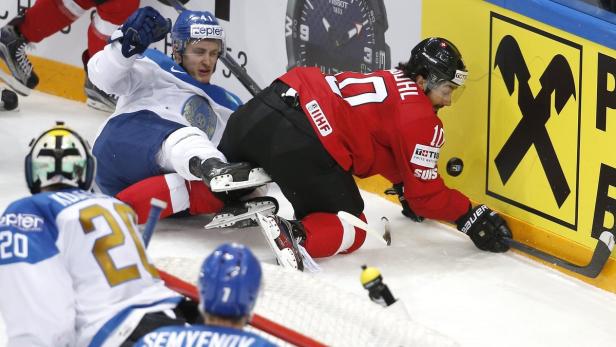Ein Schweizer Eishockeyspieler kämpft mit einem kasachischen Spieler am Spielfeldrand.