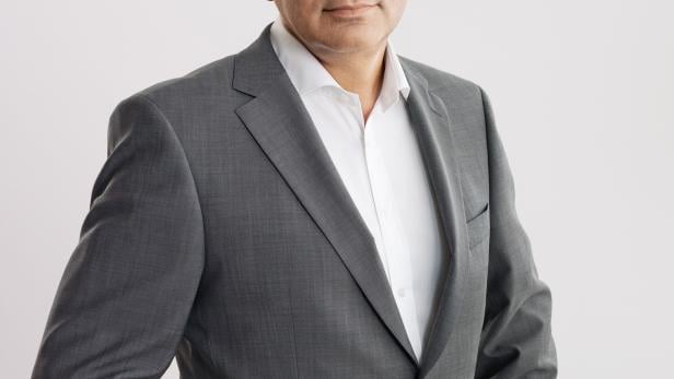 Ein Mann mit Brille und grauem Anzug posiert vor einem hellen Hintergrund.