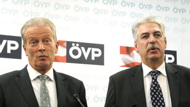 Zwei Männer in Anzügen stehen vor einem Hintergrund mit dem ÖVP-Logo.