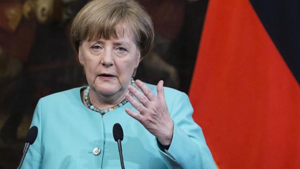 Angela Merkel gestikuliert vor einer Deutschlandflagge.