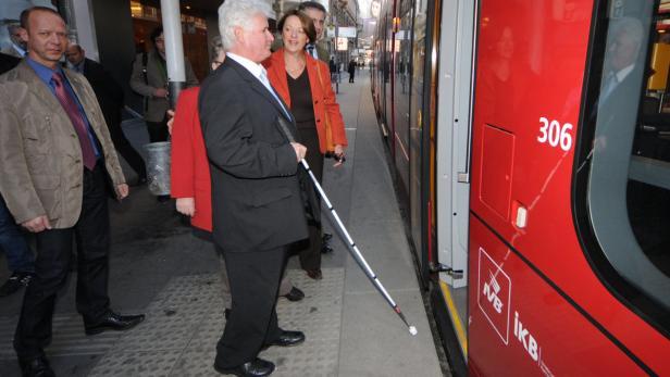 Ein blinder Mann mit Stock steigt in eine rote Straßenbahn ein.