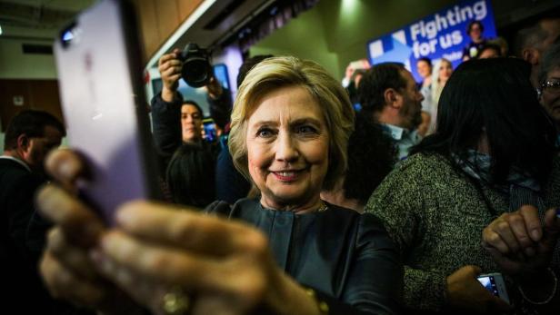 Hillary Clinton macht ein Selfie mit einer Menschenmenge im Hintergrund.