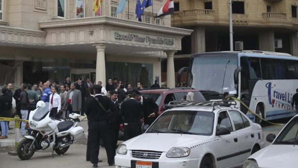 Vor dem Barceló Three Pyramids Hotel in Kairo stehen ein Bus mit zerbrochenen Scheiben und mehrere Personen.