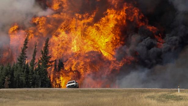Smoke and flames from the wildfires erupt behind a Smoke and flames from the wildfires erupt behind a car on the highway near Fort McMurray, Alberta, Canada, May 7, 2016. REUTERS/Mark Blinch TPX IMAGES OF THE DAY