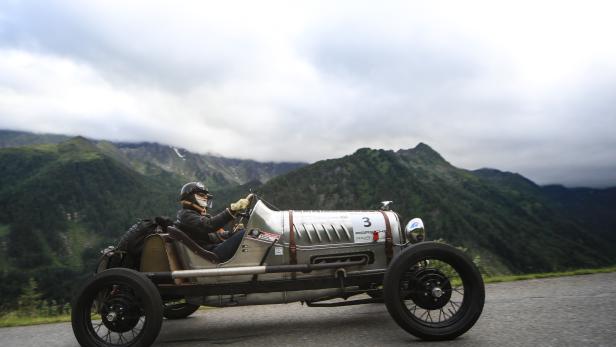 Eine Person fährt einen Oldtimer mit der Nummer 3 vor einer Bergkulisse.