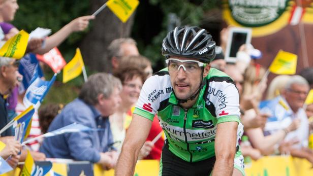Ein Radfahrer mit Helm und Brille fährt ein Rennen, umringt von Zuschauern mit kleinen Fahnen.