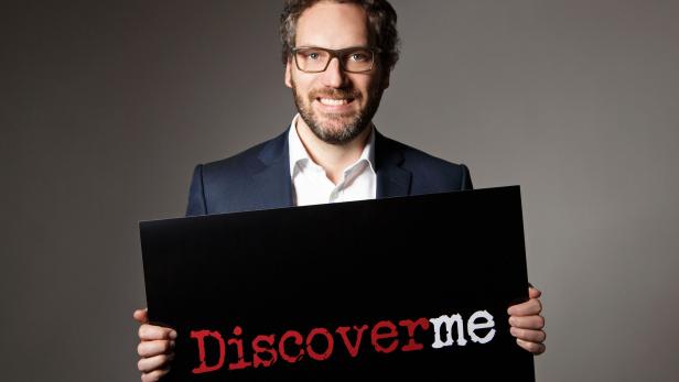 Ein Mann im Anzug hält ein Schild mit der Aufschrift „Discoverme“.