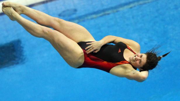 Eine Frau springt mit einem rot-schwarzen Badeanzug ins blaue Wasser.