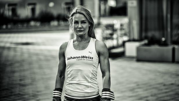 Eine Frau mit Boxbandagen und einem Sporttop mit dem Logo von Johann Weiss steht im Freien.
