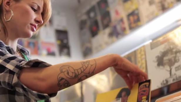 Eine Frau mit Tattoo sucht in einem Plattenladen nach Schallplatten.
