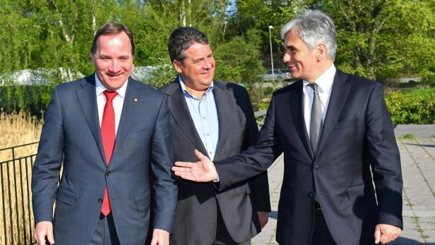 Drei Männer in Anzügen stehen im Freien und unterhalten sich.