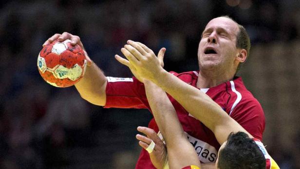 Ein Handballspieler in rotem Trikot wirft einen Ball.