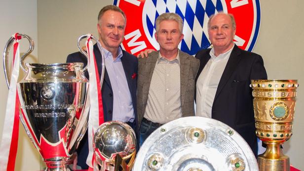 Drei Männer posieren mit den Trophäen des FC Bayern München.