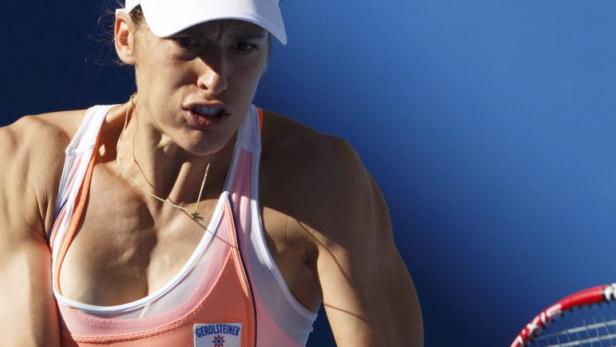 Eine Tennisspielerin mit weißer Kappe und Tennisschläger vor blauem Hintergrund.