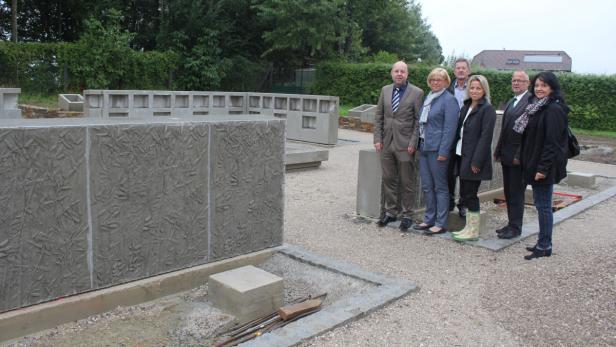 Eine Gruppe von Personen steht vor einer Betonwand mit Blattmuster.