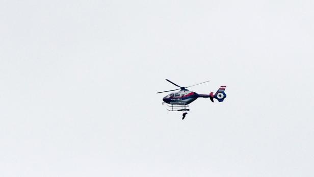 Ein Hubschrauber der österreichischen Polizei mit einer Person, die an einem Seil hängt.
