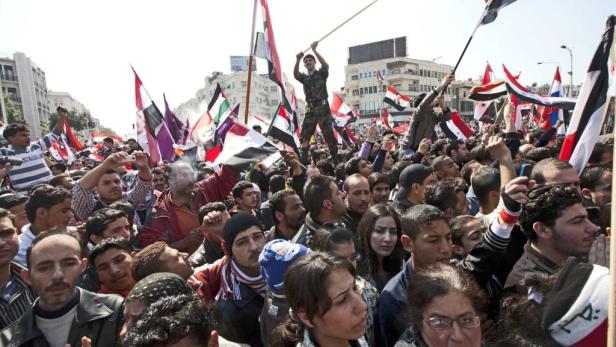 Eine Menschenmenge demonstriert mit syrischen Flaggen in einer Stadt.