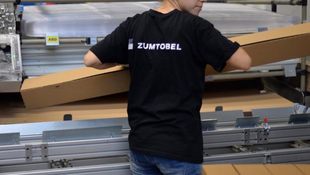 Eine Person mit einem „Zumtobel“-T-Shirt hantiert mit Kartons in einer Fabrikhalle.