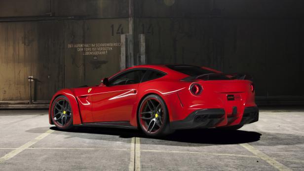 Ein roter Ferrari steht vor einer grauen Wand mit Warnhinweisen.