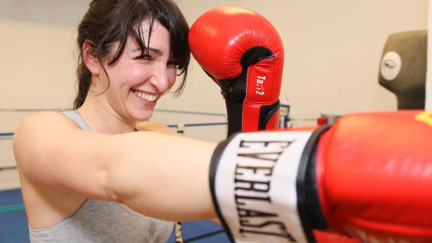 Eine lächelnde Frau mit roten Boxhandschuhen beim Boxtraining.