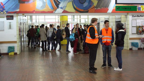 Eine Gruppe von Menschen steht in einer Halle, einige tragen orangefarbene Westen.