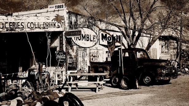 Ein verlassener Laden mit alten Werbeschildern und einem Oldtimer davor.