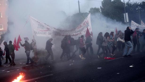 Eine Menschenmenge demonstriert inmitten von Rauch und hält rote Fahnen und ein Transparent hoch.