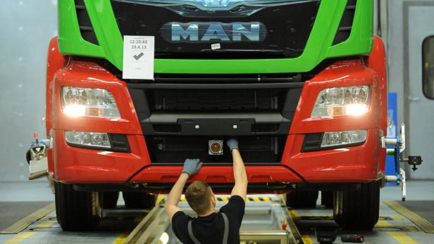 Ein Mechaniker arbeitet an der Vorderseite eines roten und grünen MAN-Lkw.