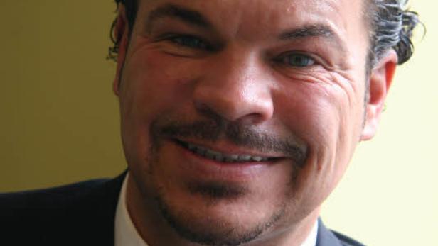 Ein Mann mit Anzug und roter Krawatte lächelt in die Kamera.