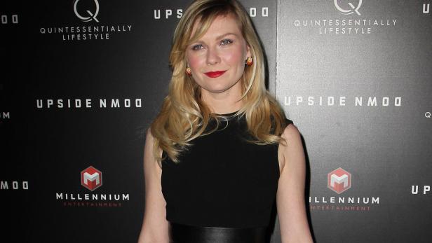 Kirsten Dunst posiert auf einer Veranstaltung vor einer Wand mit Logos.