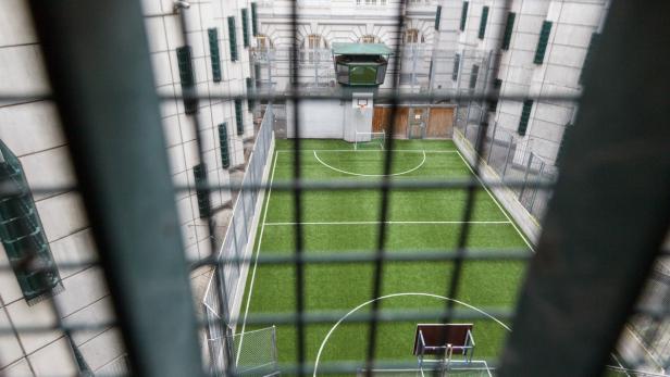 Ein Fußballfeld und ein Basketballkorb in einem Gefängnishof, gesehen durch Gitterstäbe.