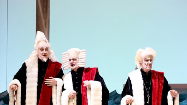 Drei als Richter verkleidete Männer stehen auf einer Bühne.