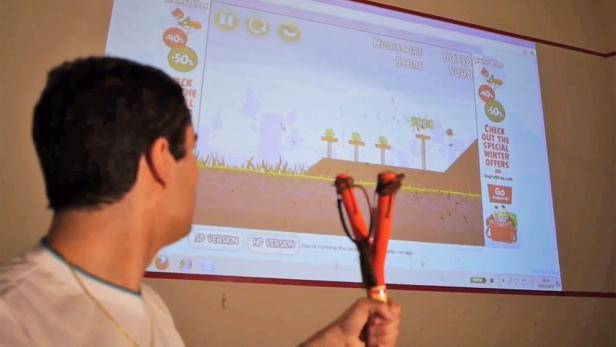 Ein Mann spielt mit einer Spielzeug-Schleuder das Spiel „Angry Birds“, das an eine Wand projiziert wird.