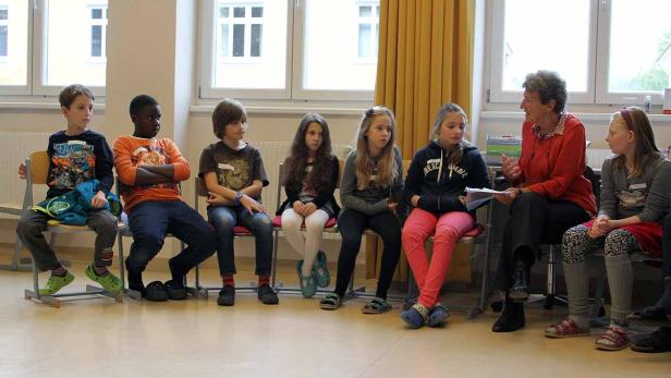 Eine Gruppe von Kindern sitzt mit einer älteren Frau im Gespräch in einem Raum.