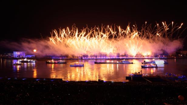Ein Feuerwerk erhellt den Nachthimmel über einem Fluss mit beleuchteten Booten.