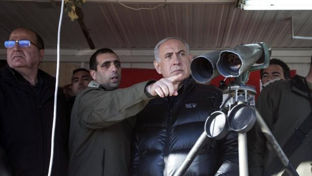 Benjamin Netanjahu blickt durch ein großes Fernglas und deutet mit dem Finger.