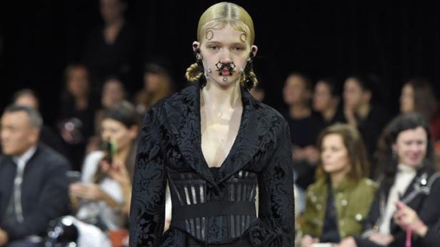 Ein Model mit Piercings im Gesicht und einem schwarzen Blazer auf dem Laufsteg.