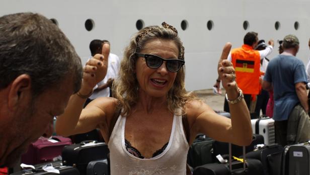 Eine Frau mit Sonnenbrille und Stirnband gibt vor Koffern ein positives Zeichen.