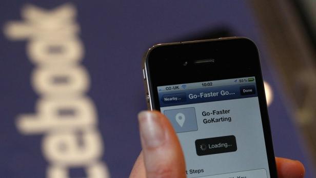 Eine Person hält ein iPhone mit der „Go-Faster GoKarting“-App vor einem Facebook-Logo.