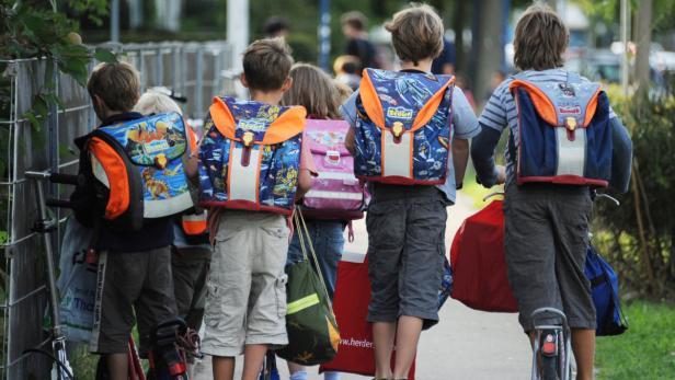 Eine Gruppe von Kindern mit Schulranzen auf dem Rücken geht die Straße entlang.