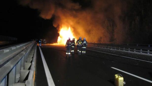 Feuerwehrleute stehen auf einer Autobahn vor einem großen Brand.