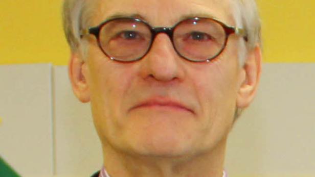 Ein Mann mit Brille, Hemd und Krawatte vor einem gelben Hintergrund.