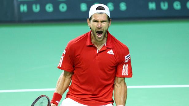Ein Tennisspieler in rotem Hemd und weißer Kappe schreit auf dem Platz.