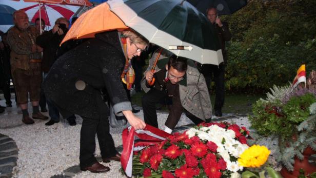 Personen legen bei Regen einen Kranz nieder.
