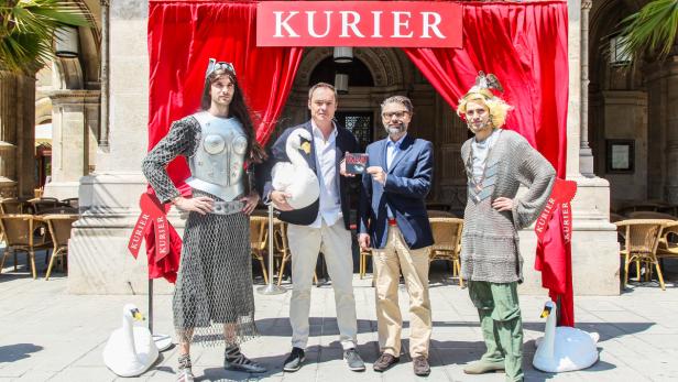 Eine Gruppe von Personen posiert vor dem „Kurier“-Gebäude mit Schwanenrequisiten.