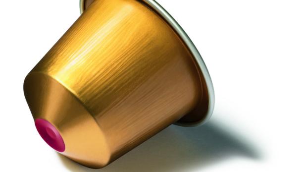 Eine goldene Kaffeekapsel liegt auf einer weißen Oberfläche.