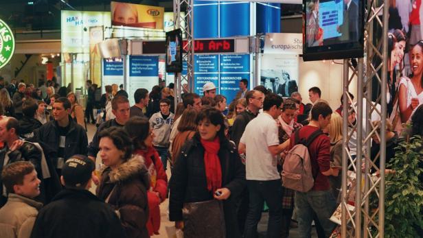 Besucher auf einer Bildungsmesse mit verschiedenen Ständen und Informationsmaterialien.
