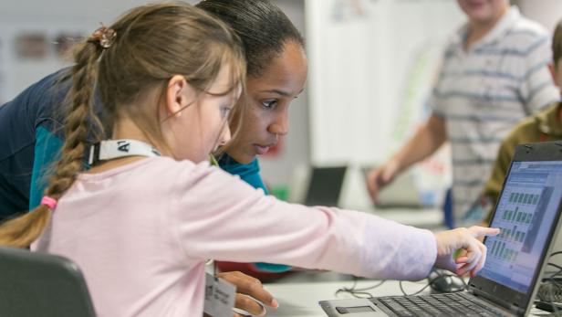 Ein Mädchen zeigt auf Diagramme auf einem Laptop, während eine Frau zusieht.